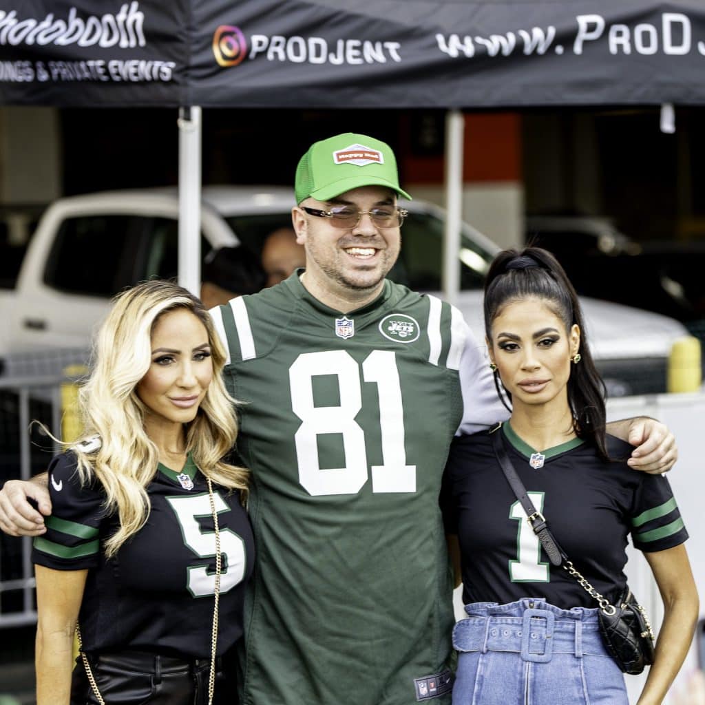 Three people pose together outdoors at a tailgate party NYC, wearing New York Jets jerseys; the man in the middle sports a green cap and jersey number 81, with two women on either side in black jerseys numbered 5 and 1.